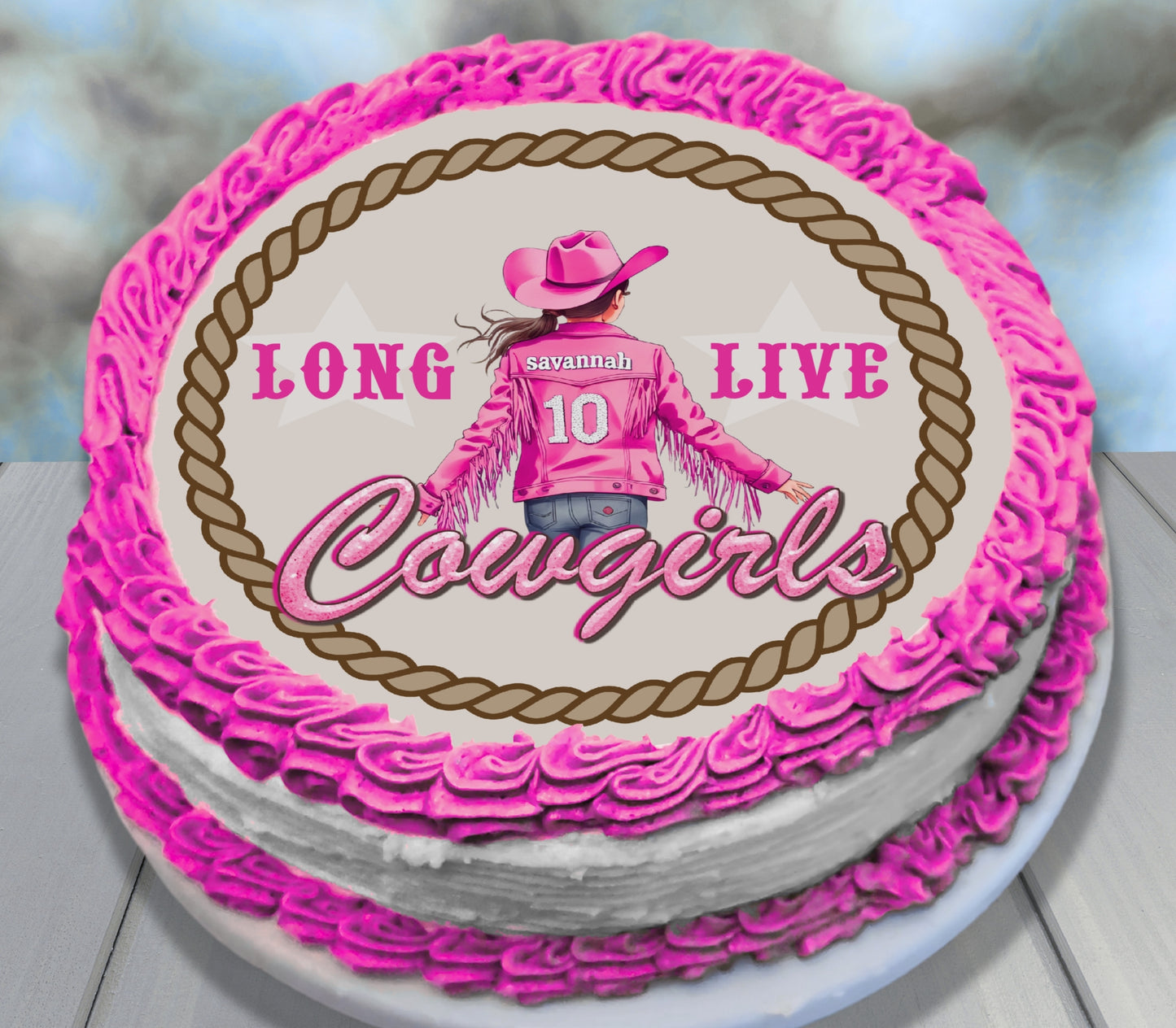 A round birthday cake decorated with bright pink frosting piped borders and a white center topper featuring a cowboy-themed graphic with the text 'LONG LIVE Cowgirls' and the name 'Savannah 10'.