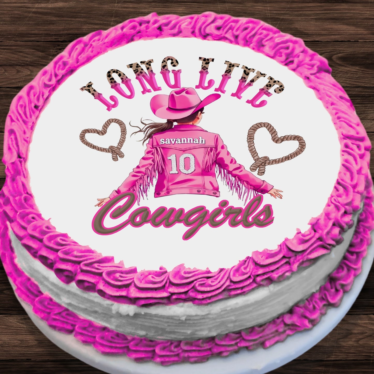 A round cake with bright pink piped frosting borders and white cake layers, topped with a custom western-themed design featuring the text 'LONG LIVE Cowgirls', rope hearts, and an illustration of a girl in a pink cowboy outfit with the name 'savannah' and number '10'.
